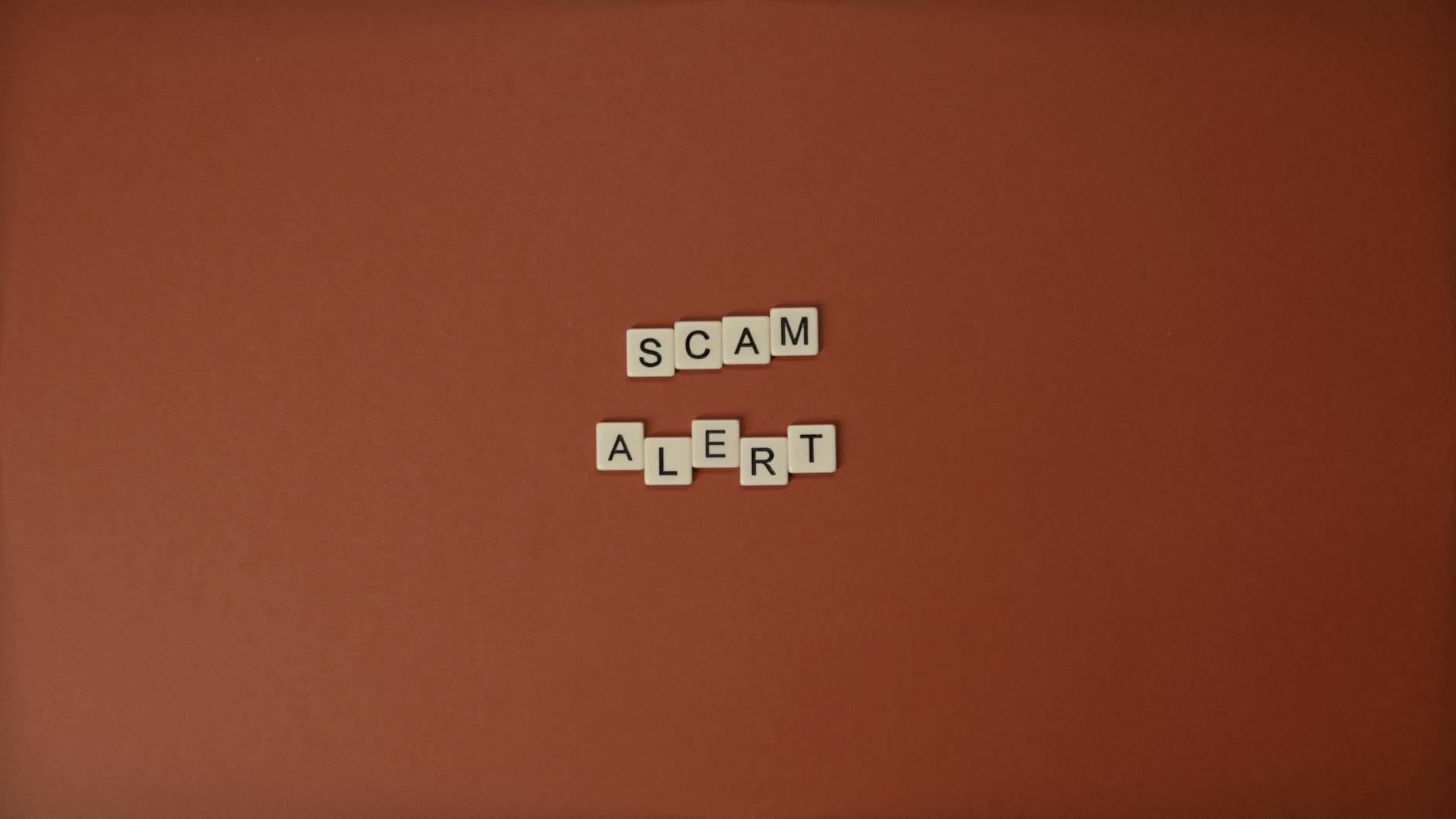 Kostki Scrabble układające się w napis Scam Alert na brązowym tle