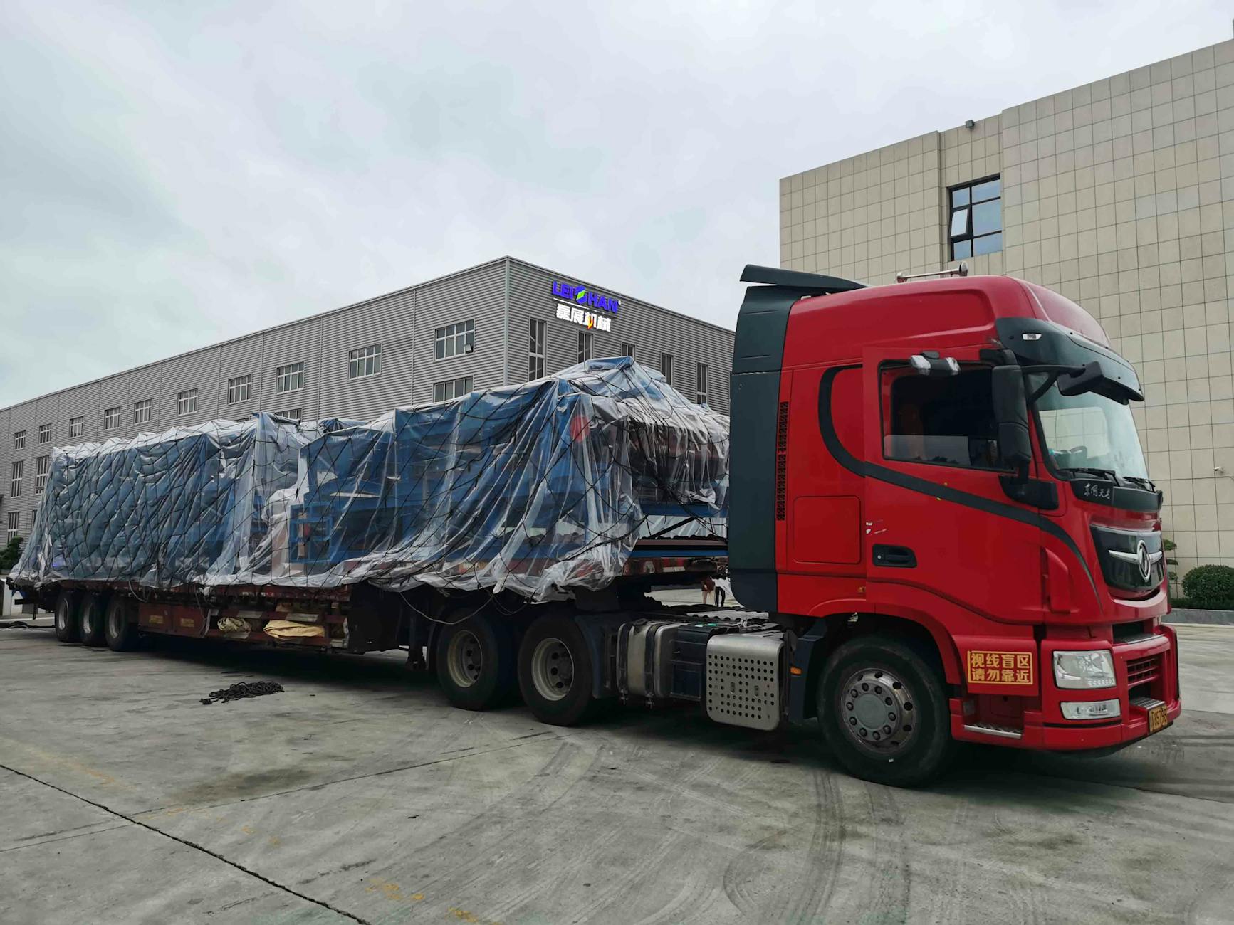 Naczepy do ponadgabarytów: semi, tiefbett, platforma – co wybrać? Czerwony zestaw ciężarowy z przykrytym ładunkiem ponadgabarytowym