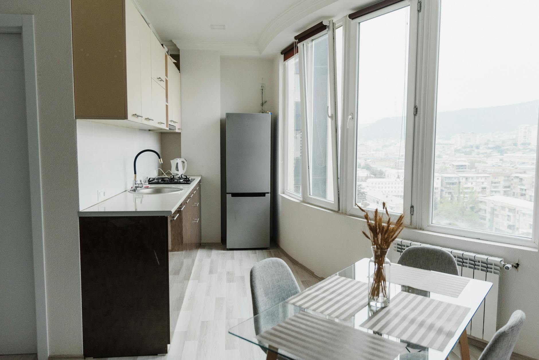 Jasna mała kuchnia w bloku z przeszklonym stołem i widokiem na miasto